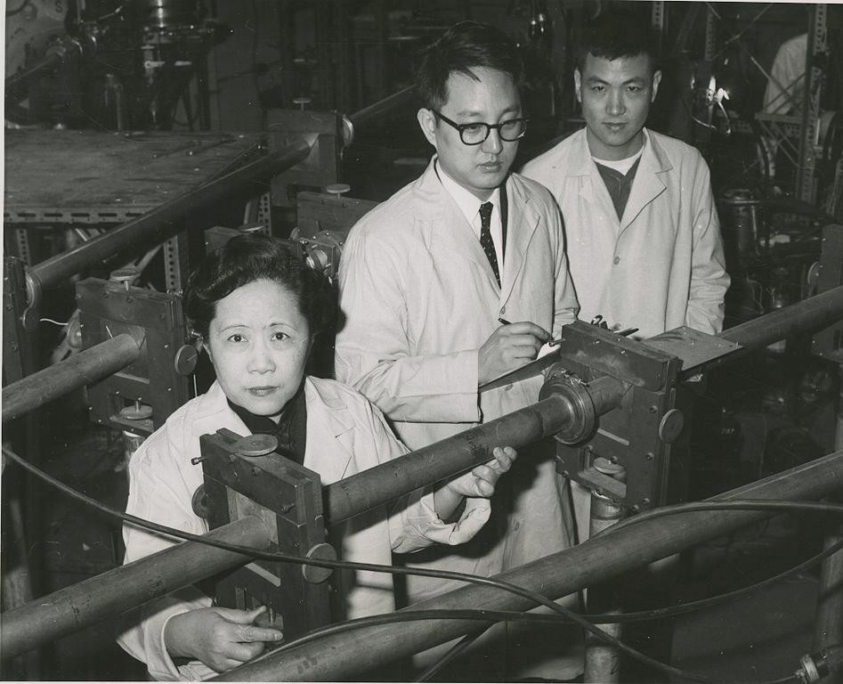 Foto da Chien Wu, à esquerda, acompanha de mais dois cientistas homens frente a uma máquina